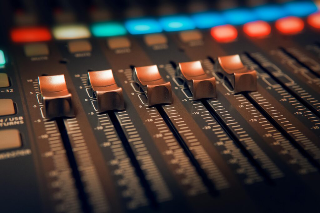 Detailed close-up of an audio mixer with illuminated controls in a studio setting.